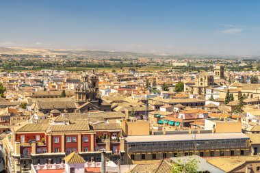 İspanya 'nın Granada kasabası. Tarihi bir şehrin panoramik manzarası, terracotta çatıları, antik mimari, ve berrak mavi gökyüzü altında genişleyen bir manzara..