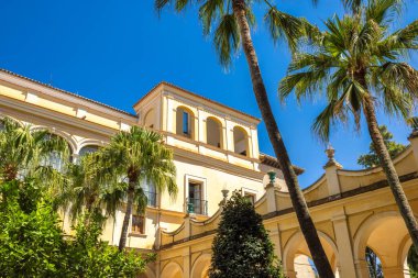 Sevilla 'nın Alcazar' ı, Sevilla kasabasındaki tarihi kraliyet sarayı, Endülüs, İspanya. Palmiye ağaçları ve sarı binası olan güneşli bir avlu. Kemerler ve balkonlar sakin bir atmosfer yaratır..