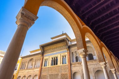 Sevilla 'nın Alcazar' ı, Sevilla kasabasındaki tarihi kraliyet sarayı, Endülüs, İspanya. Parlak mavi gökyüzü altında dekore edilmiş mimari. Karmaşık detaylar ve kemerler çarpıcı bir sahne yaratır..