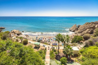 Nerja kasabası, İspanya 'nın güneyinde Endülüs' ün deniz kıyısında bir tatil beldesi. Uçurumlar ve palmiye ağaçlarıyla çevrili turkuaz suyu olan tenha bir koy. İnsanlar kumlu sahilde dinleniyor..