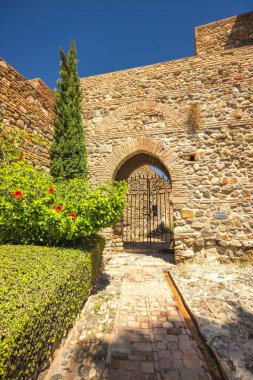Alcazaba, Endülüs, İspanya, Avrupa 'daki Malaga şehrindeki saray ve kaleler. Demir kapılı antik taş kemer yolu, yemyeşil bir yolla çevrili..