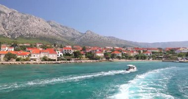 Hırvatistan, Avrupa 'daki Peljesac yarımadasının kıyısındaki Orebic kasabası. Kıyı kasabası manzarası dağları, turkuaz suları ve güneşli bir günde kıyı şeridinde beyaz dalgalar yaratan bir sürat teknesi..