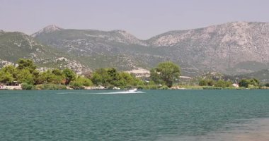 Nehrin ağzındaki Neretva nehri Adriyatik Denizi, Hırvatistan ve Avrupa 'ya akıyor. Suyun üzerinde süzülen bir jet ski ve arka planda dağlar, güneşli bir günde gölde ağaçlar..