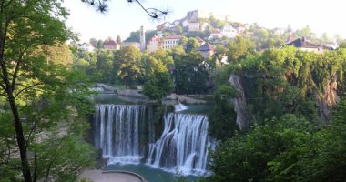 Bosna-Hersek 'in Jajce kasabasındaki Pliva Şelalesi, Avrupa. Resimli şelaleler yemyeşil bir arazide çağlıyor, arka planda tepenin üzerine kurulmuş büyüleyici bir kasaba var..