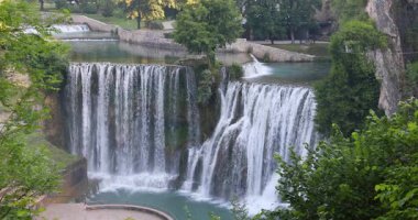 Bosna-Hersek 'in Jajce kasabasındaki Pliva Şelalesi, Avrupa. Sahne şelalesi kayaların ve yemyeşil çimlerin üzerinde çağlayarak doğanın güzelliğinin ve suyunun gücünü yakalıyor..