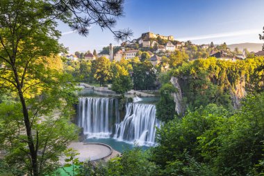 Bosna-Hersek 'in Jajce kasabasındaki Pliva Şelalesi, Avrupa. Yükselen şelale yemyeşil ile çevrili, tarihi bir kasaba ve kale arka planda bir tepenin üzerine tünemiş..