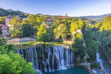 Bosna-Hersek 'in Jajce kasabasındaki Pliva Şelalesi, Avrupa. Resimli şelale yemyeşil bir çevrede şelaleye dönüşüyor. Uzaktaki sevimli bir köyün yakınında..