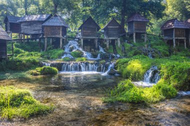 Bosna-Hersek 'in Jajce kasabası yakınlarındaki Pliva Nehri' ndeki Mlincici ahşap su değirmenleri. Tarihsel su değirmenleri çağlayan bir dere kenarında yemyeşil sularla doludur..