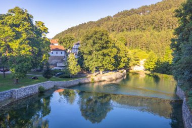 Bosna-Hersek 'in Jajce kasabasındaki Pliva nehri, Avrupa. Ağaç yansımaları ve binalarla manzaralı nehir manzarası. Huzurlu su manzaraları, yemyeşil yeşillik ve doğal güzellik gözleri cezbeder..
