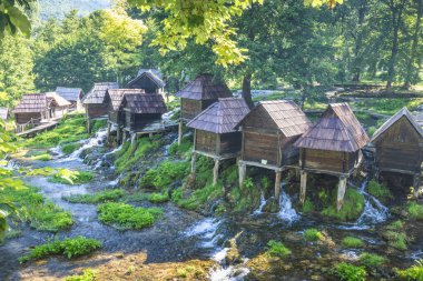 Bosna-Hersek 'in Jajce kasabası yakınlarındaki Pliva Nehri' ndeki Mlincici ahşap su değirmenleri. Su değirmenleri bir ormanda akan bir nehrin üzerinde duruyor, ahşap yapılar resim gibi bir manzara yaratıyor..