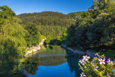 Bosna-Hersek 'in Jajce kasabasındaki Pliva nehri, Avrupa. Bereketli yeşillik ile resim gibi nehir manzarası, berrak mavi gökyüzünün altındaki sakin suyu yansıtıyor, huzurlu doğa manzarası sunuyor..