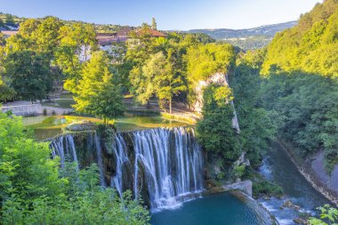 Bosna-Hersek 'in Jajce kasabasındaki Pliva Şelalesi, Avrupa. Manzaralı şelale, yemyeşil bir zemin ile çevrili turkuaz bir havuza dönüşüyor, büyüleyici binalar ve tepeler üzerine kuruluyor..