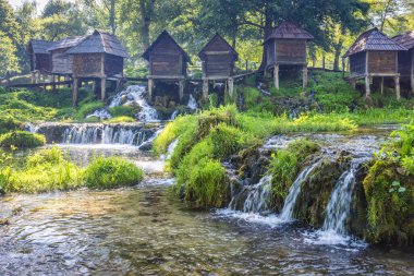 Bosna-Hersek 'in Jajce kasabası yakınlarındaki Pliva Nehri' ndeki Mlincici ahşap su değirmenleri. Kırsal su değirmenleri şelalelerin üzerine tünemiş, yemyeşil verimli doğal bir manzara yaratmışlar..