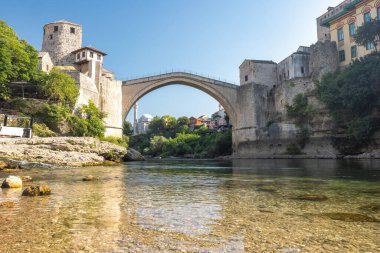 Stari Most köprüsü, Mostar kasabası, Bosna-Hersek, Avrupa 'daki Neretva Nehri üzerindeki eski köprü. Kemerli taş köprü, berrak bir gökyüzü altında antik yapıları birbirine bağlayan sakin bir nehir boyunca uzanır..