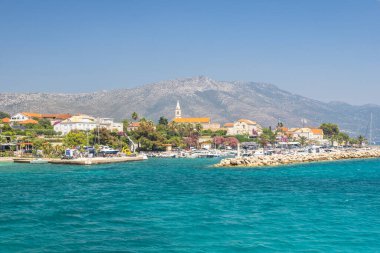 Hırvatistan, Avrupa 'daki Peljesac yarımadasının kıyısındaki Orebic kasabası. Kıyı Kasabası Panoraması: Gök mavisi deniz, dağ manzaralı büyüleyici bir kasabayla tanışır. Açık gökyüzünün altındaki limanda kayıklar sallanıyor.