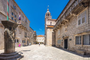 Korcula, Hırvatistan - 11 Temmuz 2024: Korcula adası. Taş binaları ve açık mavi gökyüzünün altında yüksek bir kilise kulesi olan Avrupa şehir meydanı, tarih ve cazibe yayıyor..