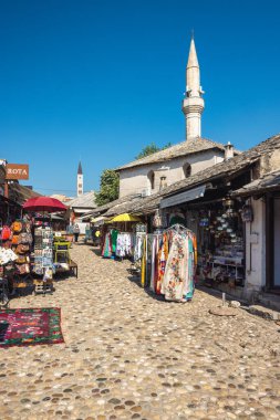 Mostar, Bosna-Hersek - 9 Temmuz 2024: Mostar 'da açık mavi gökyüzüne karşı geleneksel el sanatları ve İslami mimari çalışmaları ile hareketli pazar. Güzel tarihi manzara.