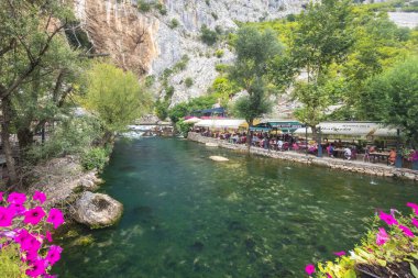 Blagaj, Bosna-Hersek - 9 Temmuz 2024: Blagaj Tekke manastırı yakınlarındaki Buna Nehri. Resimli nehir kenarı restoran sahnesi kayalık yamaçlara kurulmuş yemyeşil bitki örtüsü ve akan nehir kenarına..