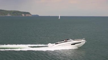 Sopot, Polonya - 2 Mayıs 2025: Baltık Denizi kıyısındaki sahil beldesi. Modern motorlu tekne okyanus dalgalarını keser, uzak, yeşil bir sahil şeridine doğru ilerlerken beyaz bir iz bırakır..