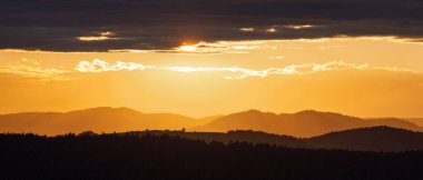 Sunset over rolling hills with a dramatic sky. Warm light casts long shadows, creating a serene and scenic landscape.
