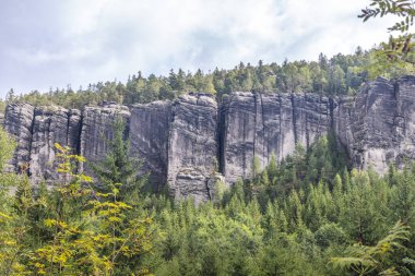 Adrspach-Teplice Rocks, sandstone formations in Hradec Kralove Region in the Czech Republic, Europe. Jagged rock formations reach skyward, standing guard over a lush green forest under a cloudy sky.