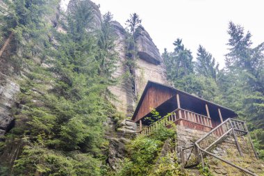 Landscape of Adrspach-Teplice Rocks area, in Hradec Kralove Region in Czech Republic, Europe. Wooden cabin nestled amidst towering rock formations and lush evergreen trees in tranquil natural setting.
