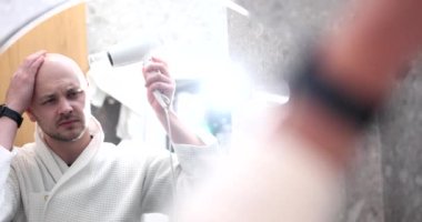 Kel genç adam saç kurutma makinesiyle kafasını kurutuyor. Erkek şablonu kellik kavramı