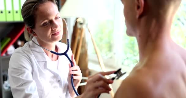 医者は胸の聴診器を通して若い男性患者の呼吸と心を聞く 肺炎咳や肺の喘鳴 — ストック動画