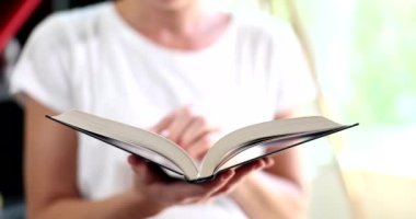 Kadın rahat oturma odasında kitap okuyor ve sayfayı çeviriyor. Eğitim görmek, kitap okumak ve evde kalmak.
