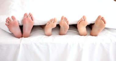 Yatakta iki erkekle yatan kadın bacakları. Aldatma ve aşk üçgeni