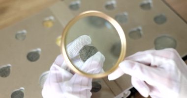Beyaz eldivenli Numismatist büyüteçle eski parayı inceliyor. 4K film yavaş çekim. Hobi ayrımcılık konsepti