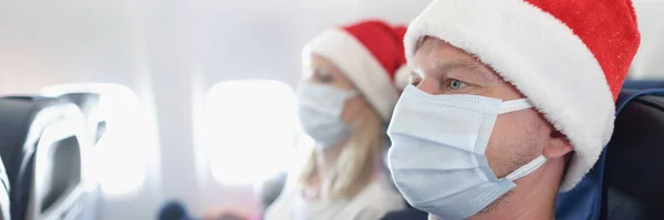 Man and woman in santa hats and protective face masks flying in airplane. New Year journey during covid 19 pandemic concept