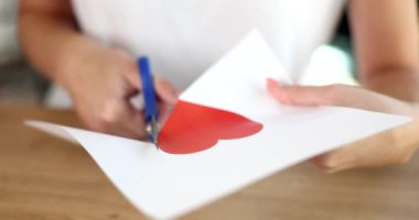 Kırmızı kalbi kesen kadın makasla 4K 'lık filmi yavaşlatıyor. Sevgililer Günü konsepti için el yapımı kartpostallar 