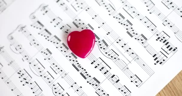 红色玩具心脏躺在音乐笔记上 特写4K电影慢动作 写情歌的概念 — 图库视频影像