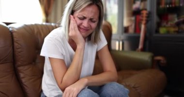 Sağlıksız kız evdeki kanepede oturur ve diş ağrısından dolayı yanağına dokunur. Mutsuz, sağlıksız bir kız, dişlerindeki ani ağrıdan dolayı kendini iyi hissetmiyor.