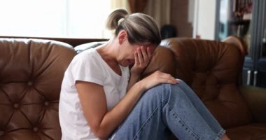 Depresyondaki genç kadın evde tek başına ağlayan elleriyle yüzünü örtüyor. Üzgün, ağlayan kız kanepede oturuyor.