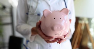 Steteskoplu doktor hemşire elinde pembe domuz kumbarası tutuyor. Sağlık sigortası ve sağlık ve ilaç