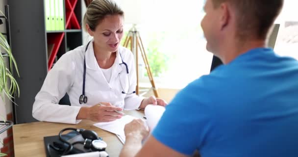 女性医師は病院で会う男性患者に助言する フレンドリーな医師が話し 診察や症状についてのアドバイス — ストック動画