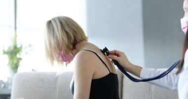 Doktor, koruyucu maskeli bir kadının ciğerlerindeki hırıltıyı dinliyor. Zatürree ve bronşit tedavisi kavramı
