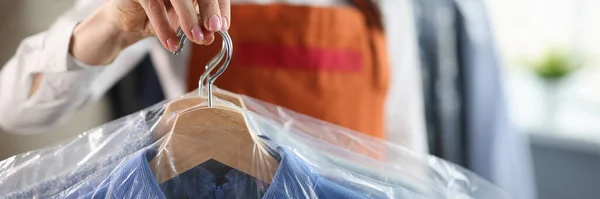 Administrator at dry cleaners keeps clean clothes on hangers in bag. Laundry and dry cleaning services concept