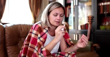 Burun spreyi kullanan hasta genç bir kadın evdeki kanepede oturan akıcı bir burnu tedavi ediyor. Yetişkinlerde mevsimsel grip ve akışkan burun rhinitis