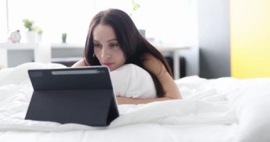Evde yatakta yatarken tablet üzerinde çalışan yorgun bir kadın. İş konseptinde kötü haberler ve hatalar