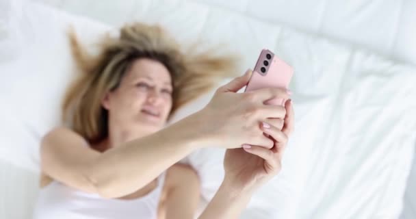 微笑的漂亮女人看着智能手机屏幕 躺在床上 床上概念的成功自拍 — 图库视频影像