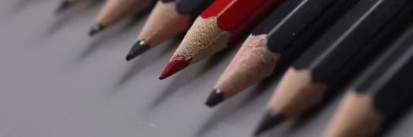 Close-up of one red pencil between row of black pencils. Stand out from crowd, not like everyone else and individuality concept
