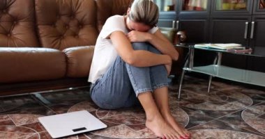 Terazinin yanında oturan bir kadın ağlıyor, yakın plan, yavaş çekim. Kavramsal kilo alma, başarısız diyet