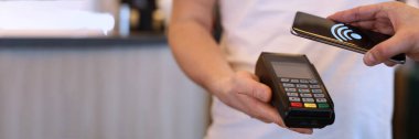 NFC teknolojisiyle pos terminali üzerinden cep telefonuyla ödeme yapan adamın yakın çekimi. Kablosuz para transferi için akıllı telefon kullanan bir adam. Kahve faturasını ödeyen müşteri.