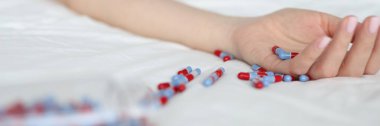 Close-up of young woman committing suicide by overdosing on medication. Overdose pills and addict. Female lying on bed and scattered pills on bedclothes