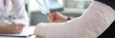 Close-up of man with broken arm at doctor appointment. Doctor at hospital prescribing treatment. Injury, accident, healthcare and medicine concept