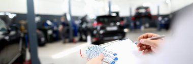 Close-up of male worker writing machine diagnostic data in garage. Fixed car after maintenance in service. Pit stop, service station and handyman concept