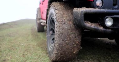 Kirli tekerlekleri olan kırmızı araba kırsal yolda duruyor. Yakın çekim 4K film ağır çekim. Off-road sürüş konsepti 